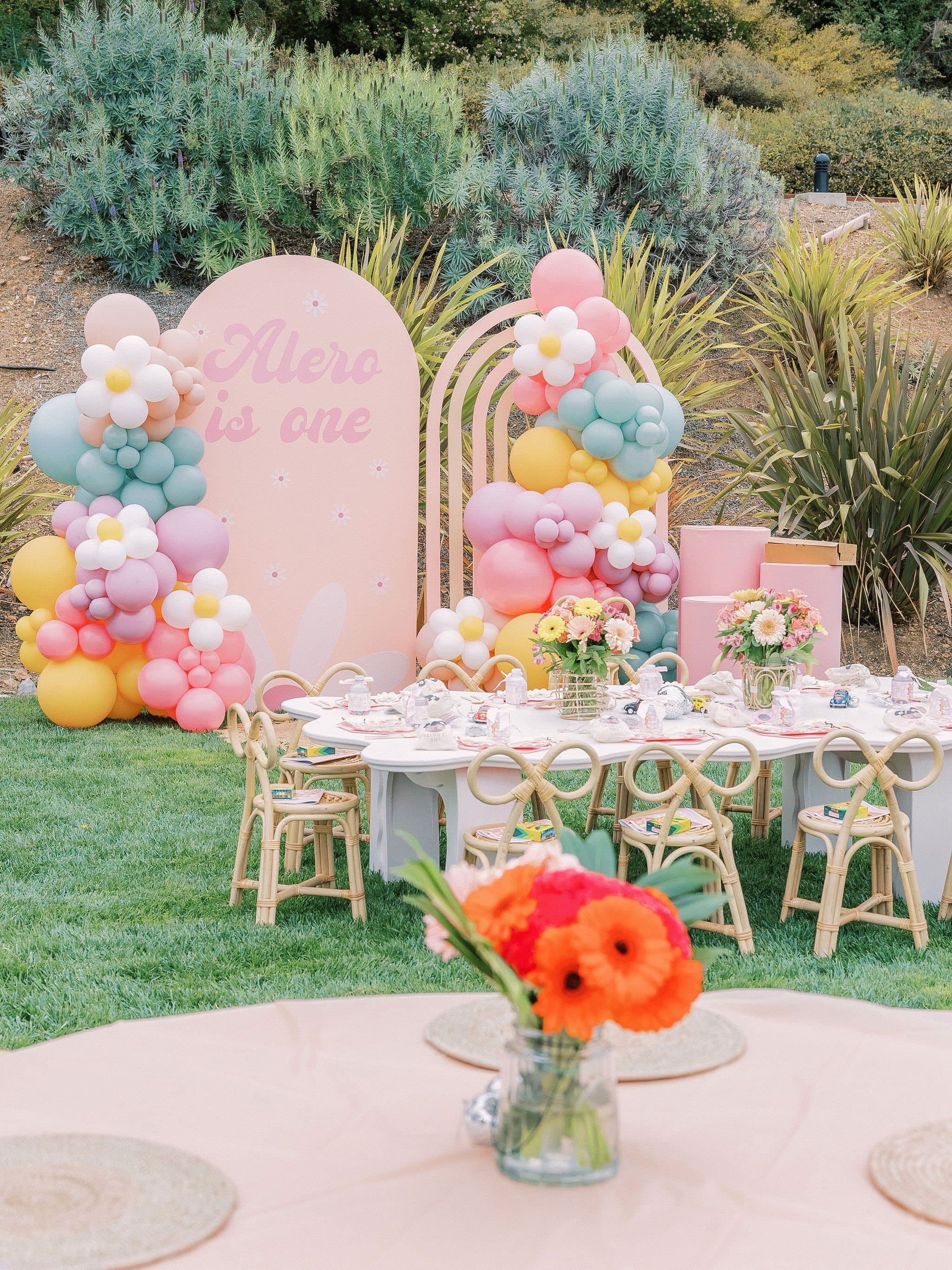 Pastel balloon arch, kids table and rattan chairs at a first birthday