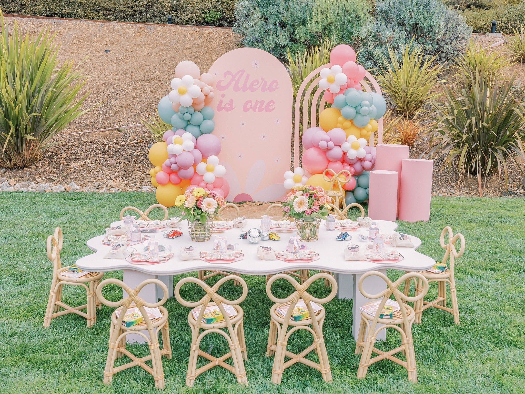 Pastel first birthday tablescape with rattan chairs and a balloon arch