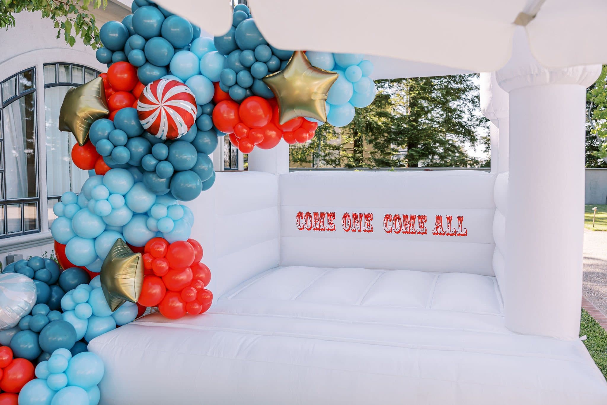 White bounce house with red and blue carnival balloons
